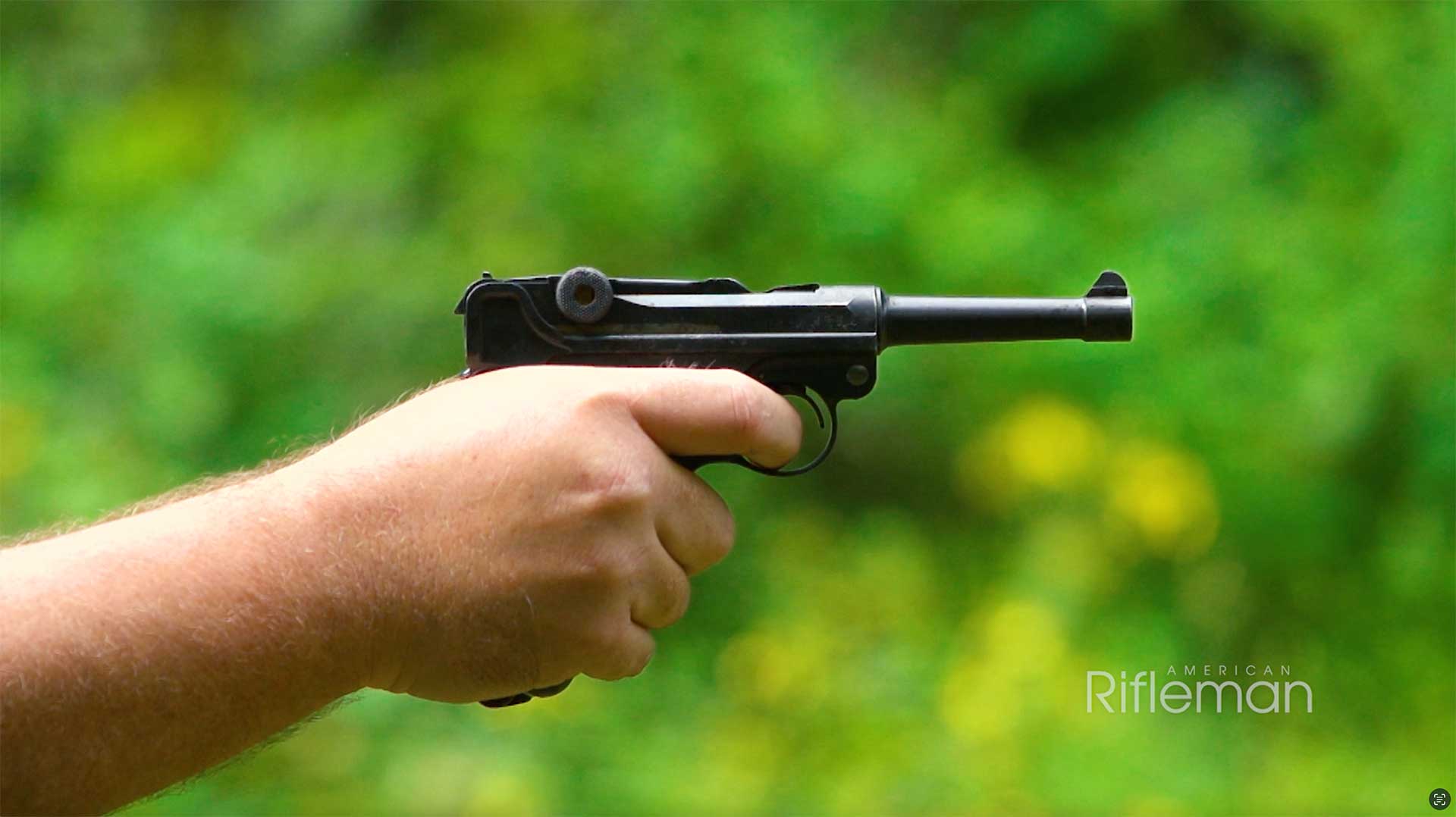 Man aiming a Luger pistol on an outdoor range.