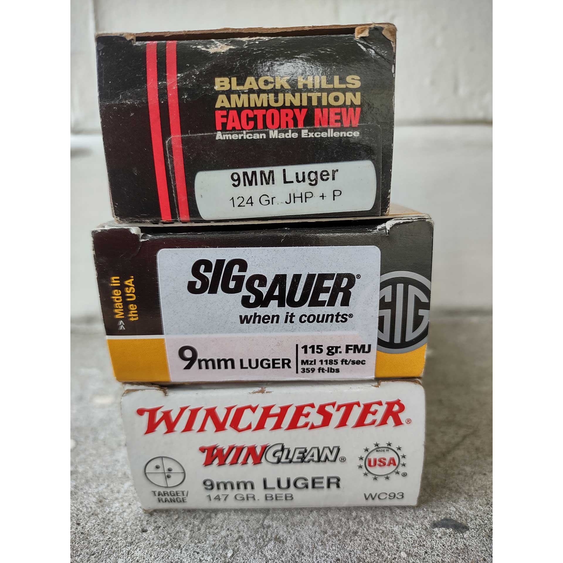 A stack of 9mm Luger ammunition boxes, including Winchester, SIG Sauer and Black Hills cartridges.