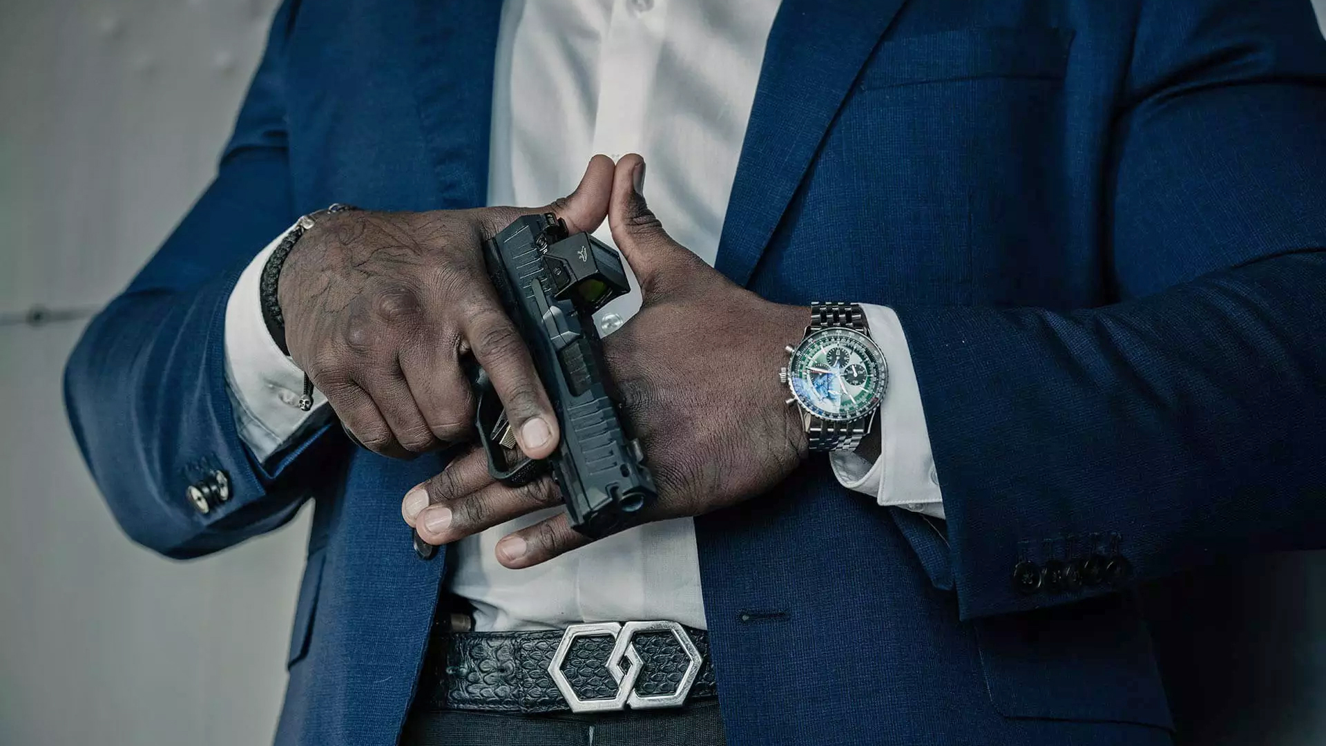 Man in a suit wearing a watch and posing with the Canik Mete MC9 Prime pistol.