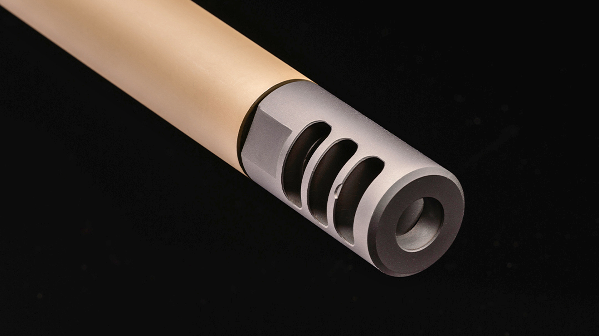 Black muzzle brake on the end of the tan-colored Watchtower Bridger rifle barrel.