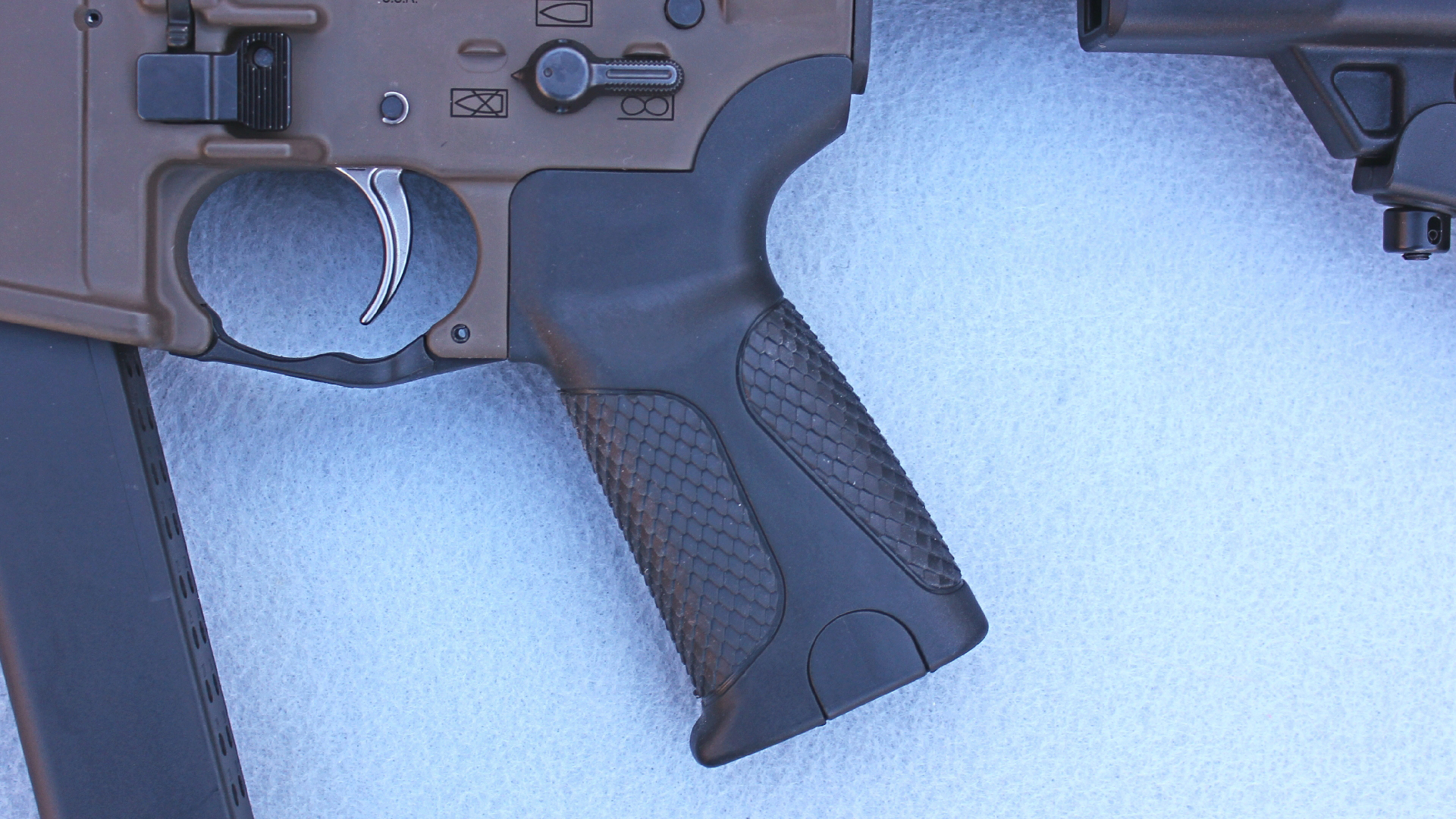 LWRCI IC 9 Carbine rubberized black grip attached to lower receiver rear of silver-color trigger bow