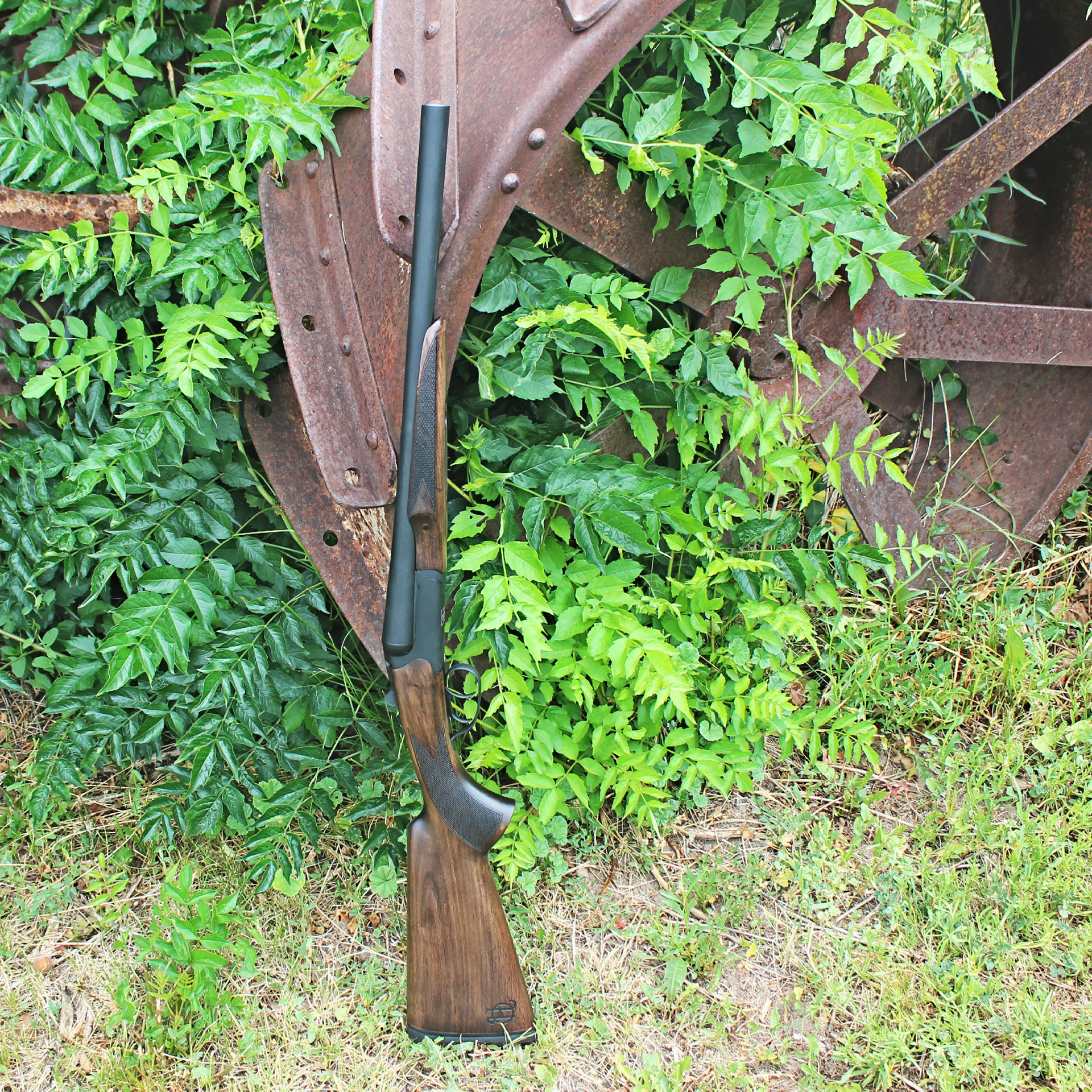 Heritage Badlander shotgun side-by-side coach gun resting on rusty metal wheel outdoors bushes