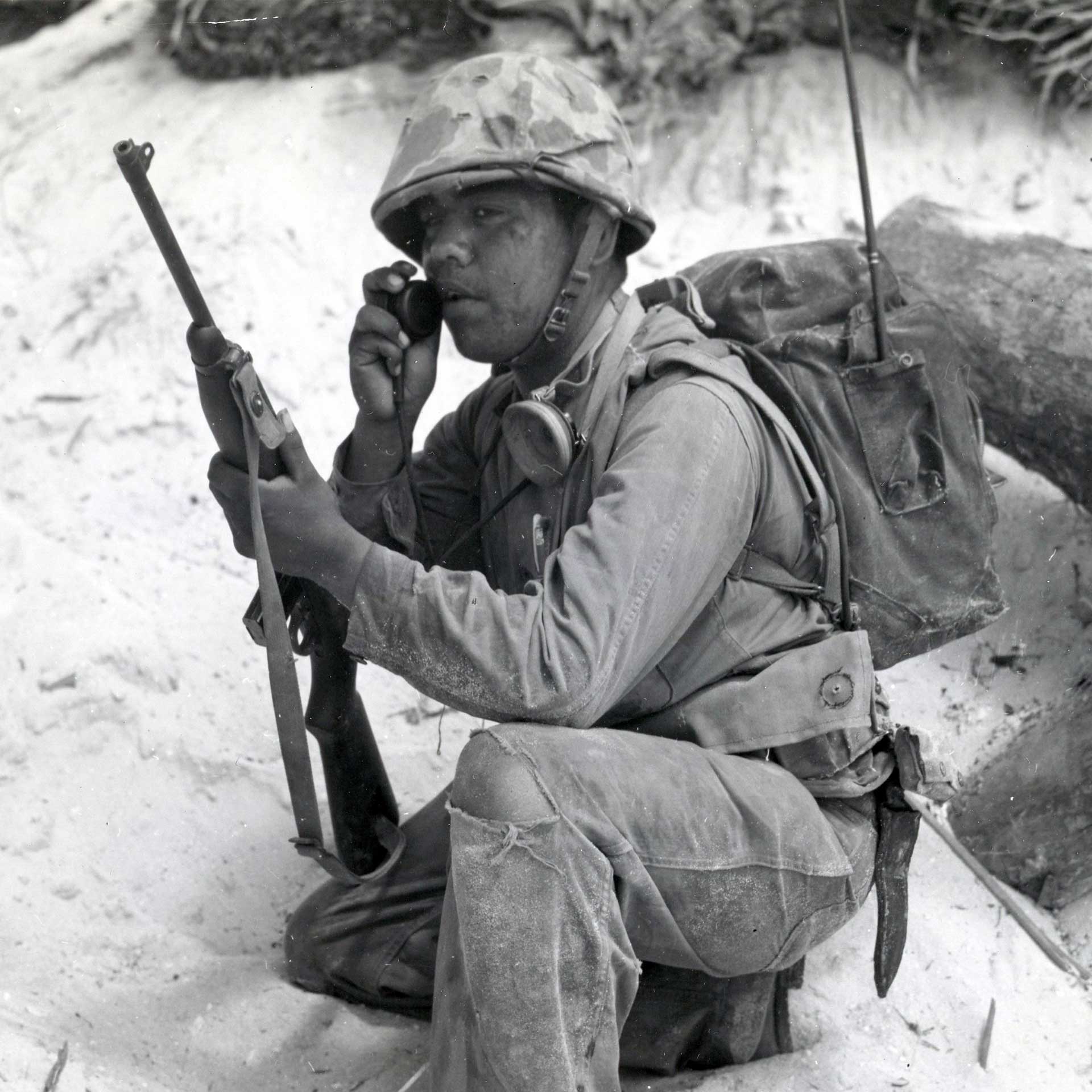 A U.S. Marine radioman makes a call on the beach at Tarawa while holding an M1 carbine.