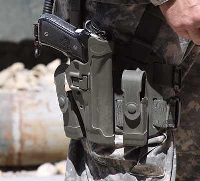 A Beretta M9 inside a polymer holster mounted on a camouflage pant leg.