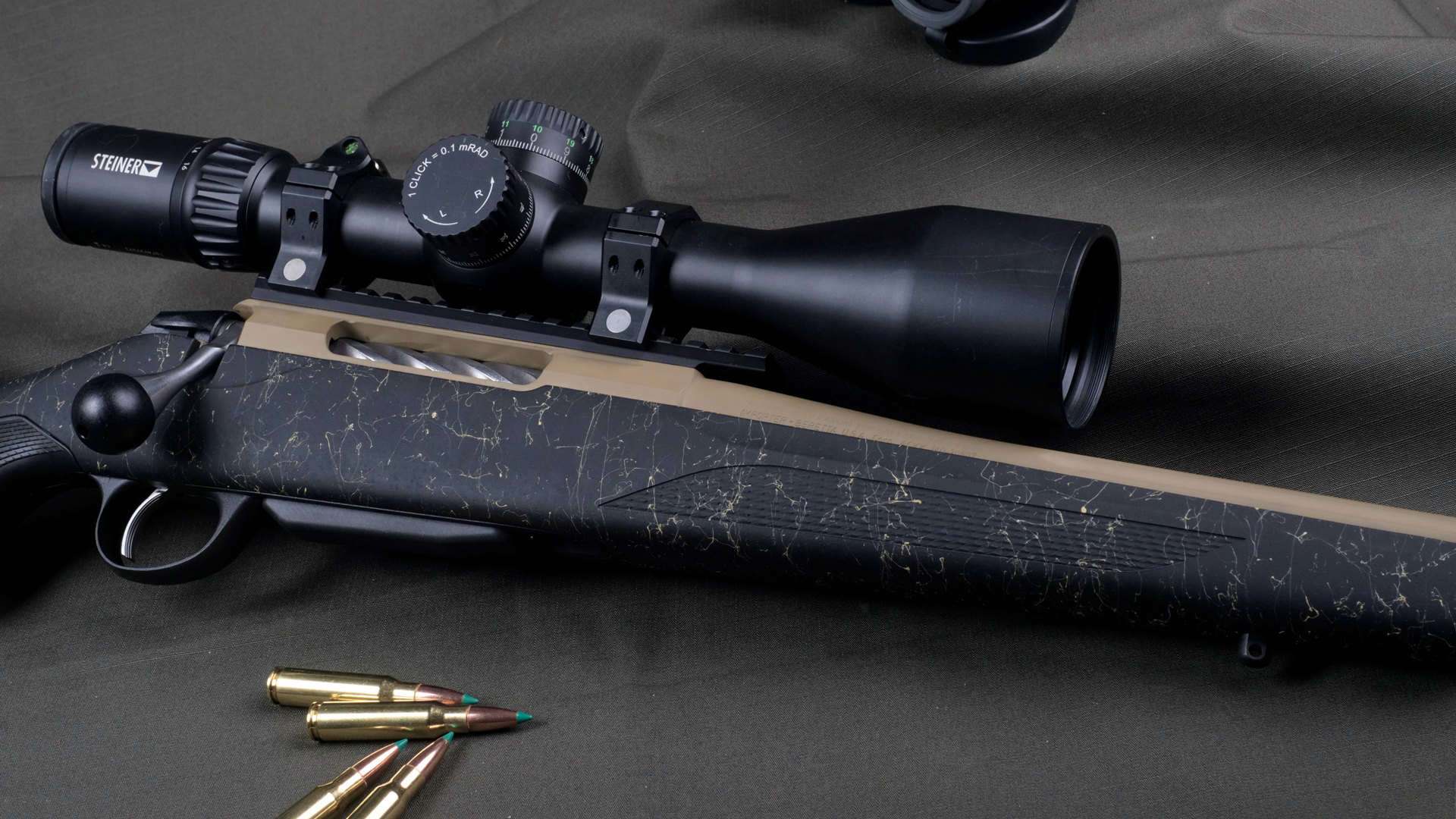 Tikka T3x Superlite bolt-action hunting rifle right-side mid-section view tan barrel action black spider-web texture stock shown on green fabric with binoculars riflescope ammunition