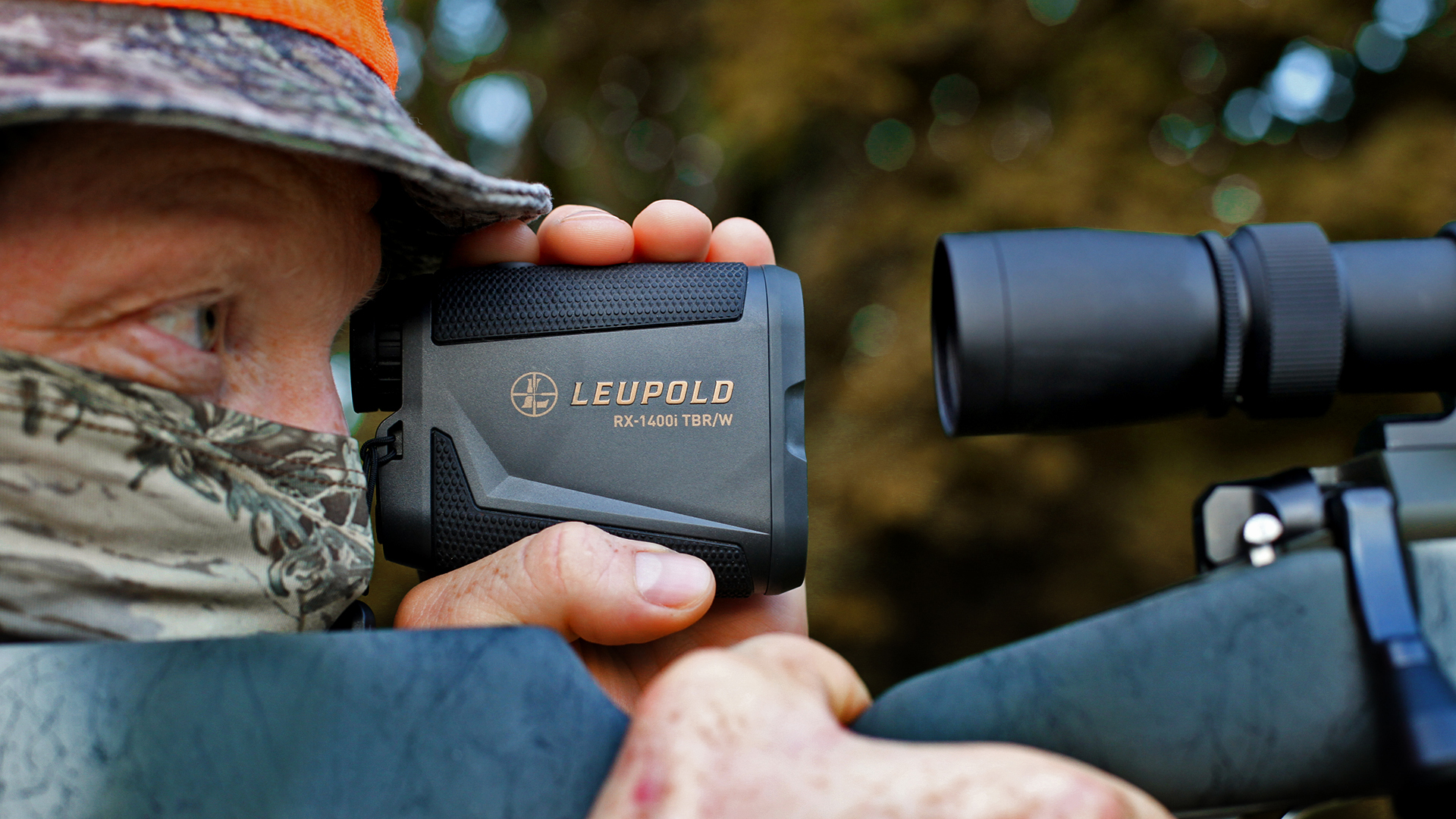 Camouflaged hunting blaze orange safey using Leupold rangefinder in the field with rifle