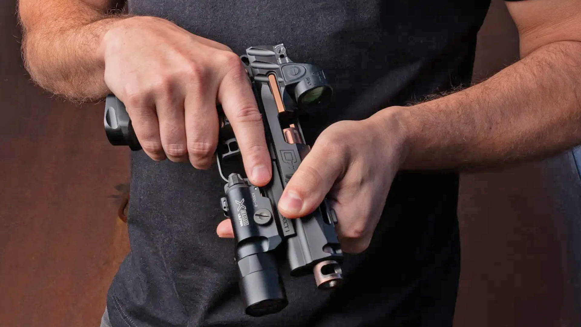 A man handling the Wilson Combat Division 77 Project 1 handgun, featuring a weapon-mounted light and red-dot optic.