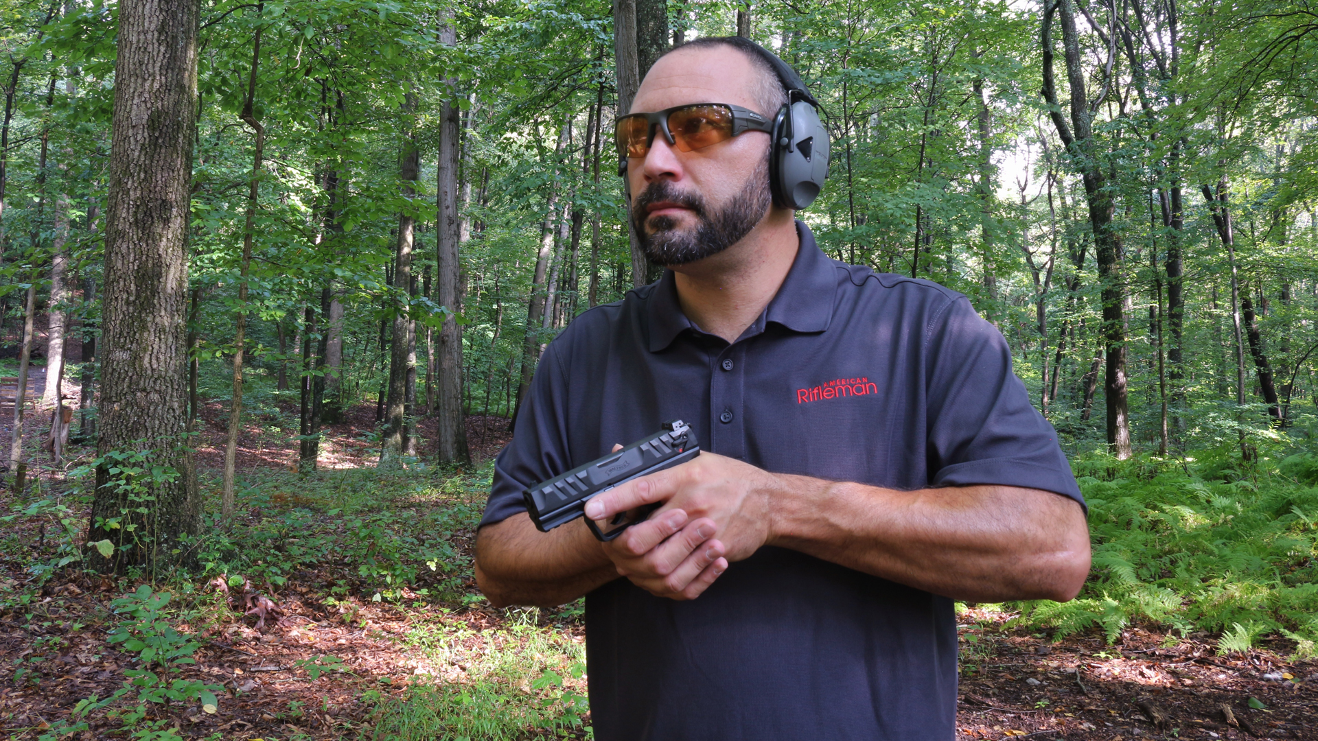 Author Frank Melloni holding Walther PD380 semi-automatic black pistol mid-chset outdoors wearing protective shooting gear glasses earmuffs