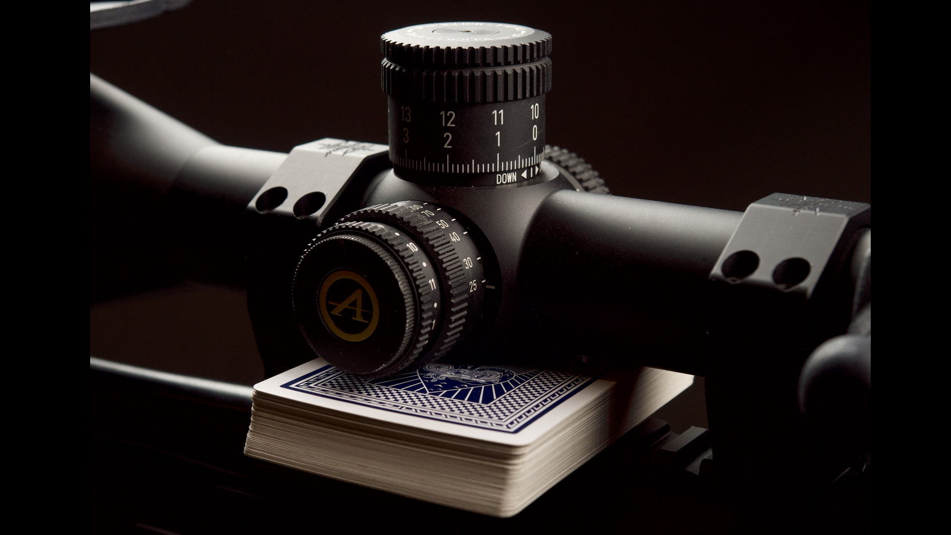 Black riflescope lit from above with a deck of playing cards beneath to set level