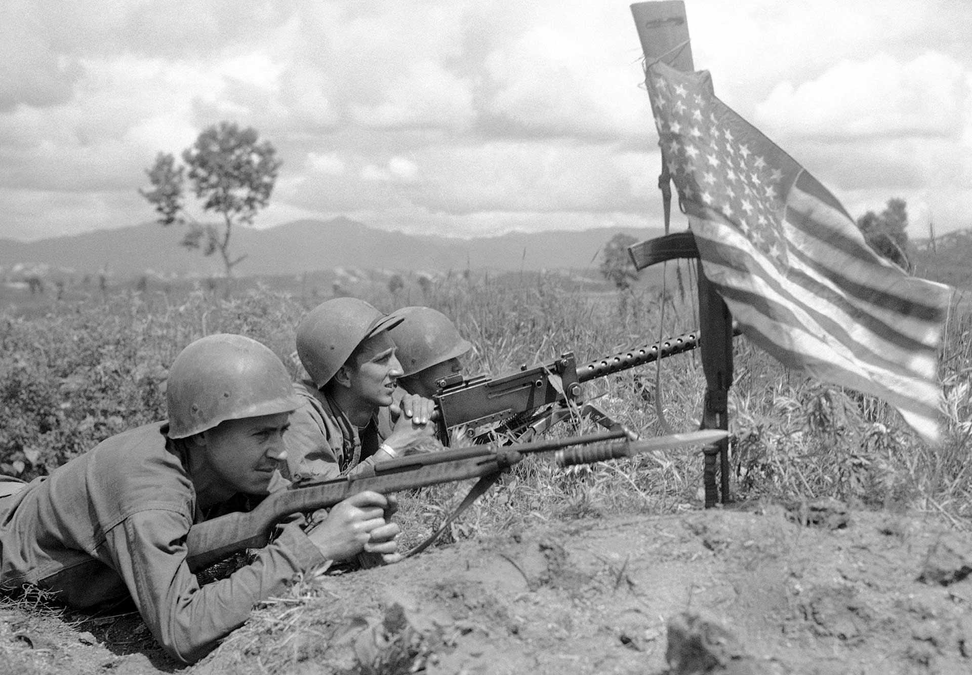 Three U.S. Army soldiers laying prone behind an American flag in Korea.