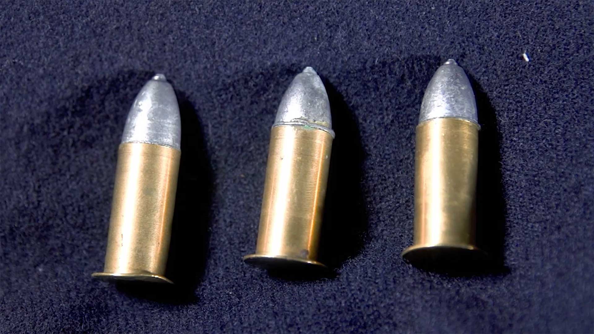 Three Maynard carbine cartridges arrayed on a blue cloth background.