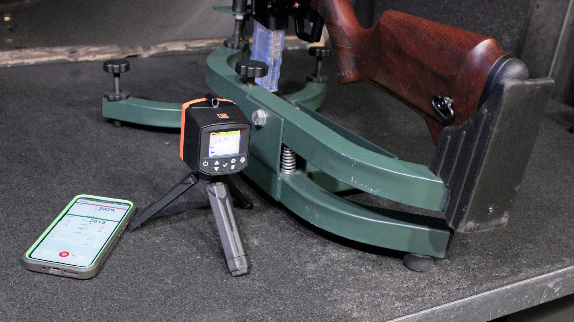 Labradar LX chronograph shown on tripod between wood stock rifle and telephone