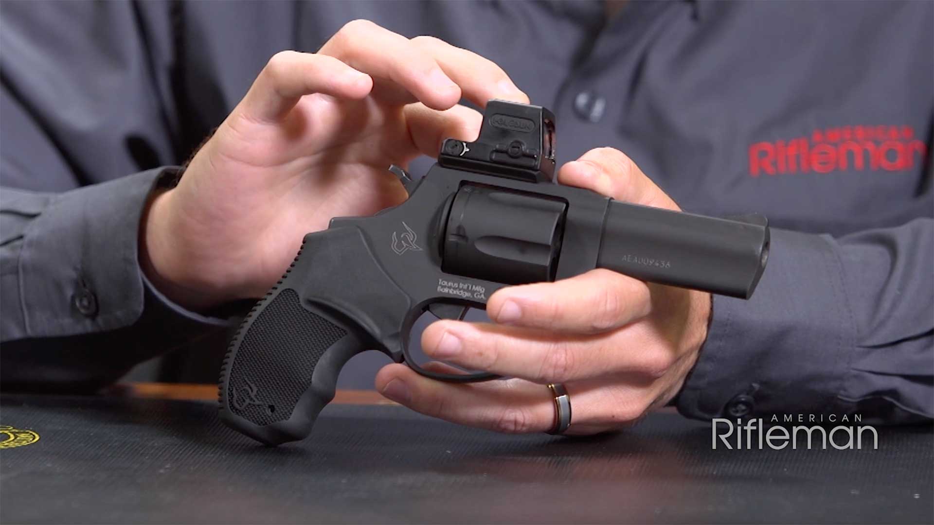 Man pointing at a mounted optic on top of the all-black Taurus 605 T.O.R.O. revolver.