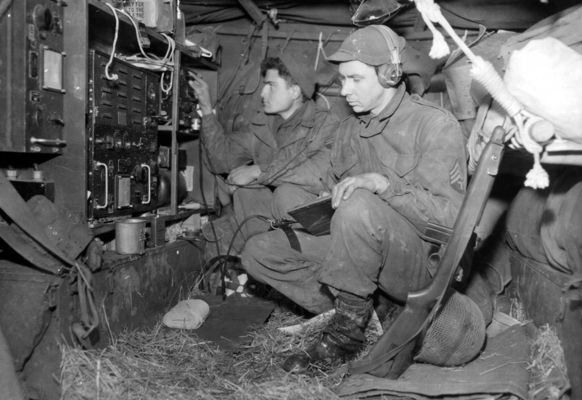 Communications troops of the 76th Infantry Division making calls with an M1 carbine propped up next to them.