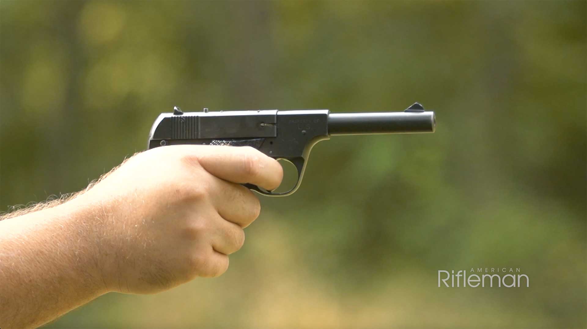 A man aims a Hi-Standard Model B pistol on an outdoor range.