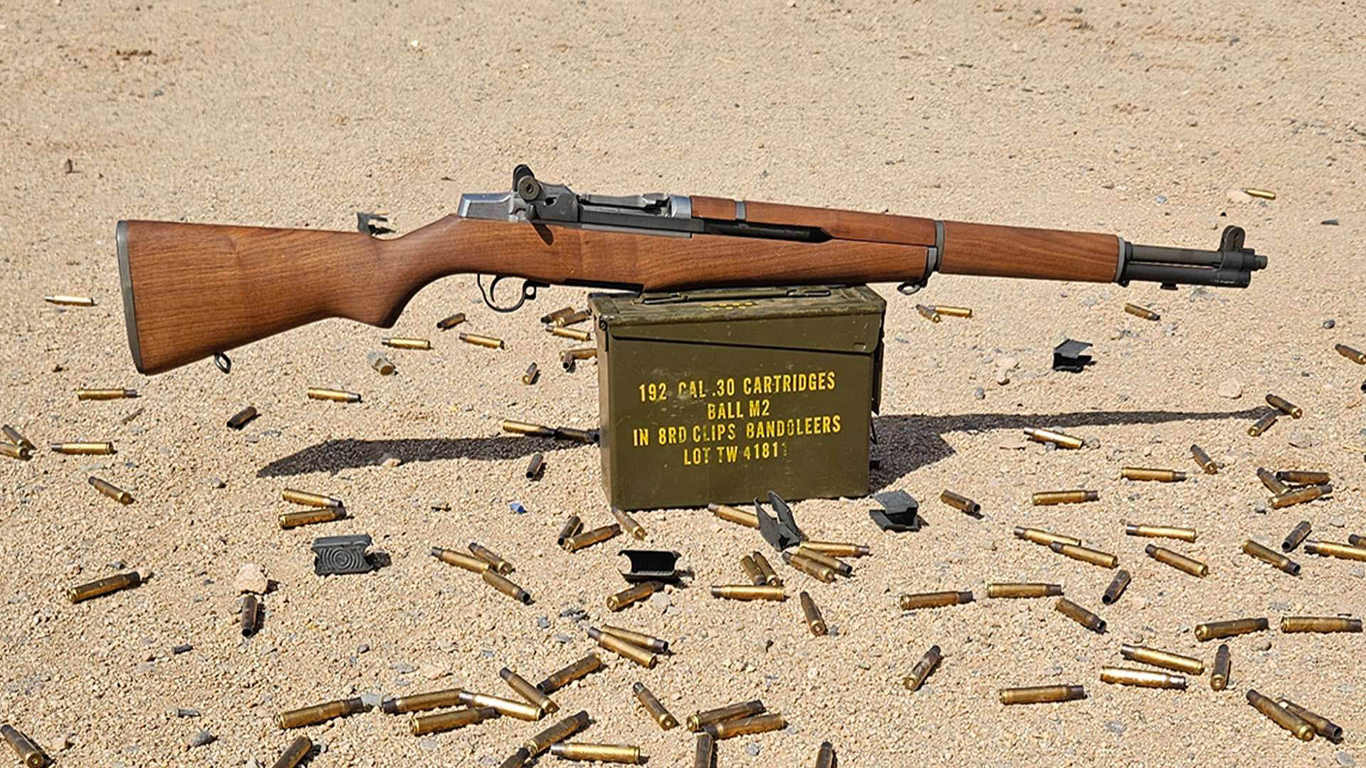 M1 Garand wood stock rifle right-side view shown on ammo can with spent cases scattered below outdoors
