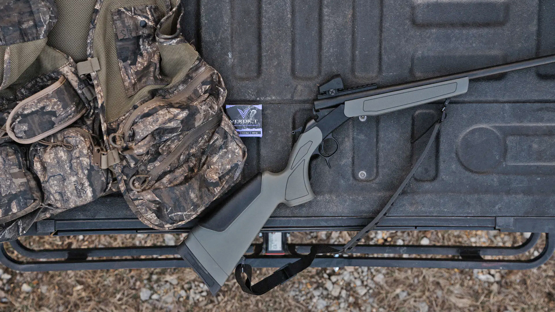 A CVA Scout Spur single-shot shotgun sitting on a truck bed, next to camouflage hunting equipment.