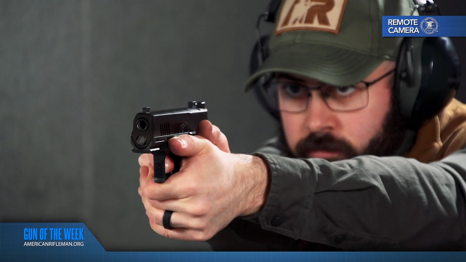 GUN OF THE WEEK REMOTE CAMERA text on image of man wearing ballcap headphones glasses beard shooting black kimber r7 mako carbon compact optic ready 9 mm pistol indoors