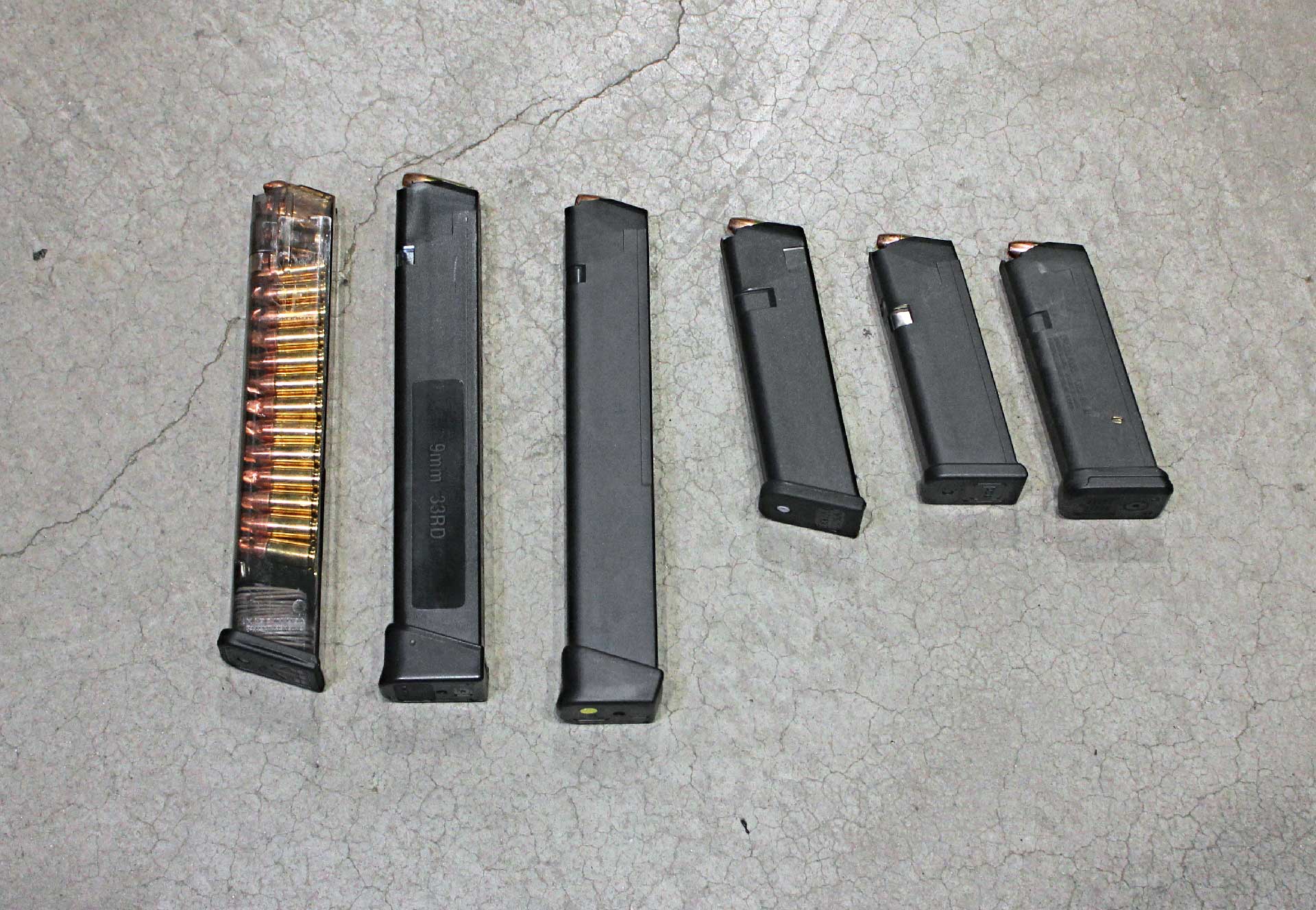 A selection of Glock-compatible handgun magazines shown on a concrete floor.