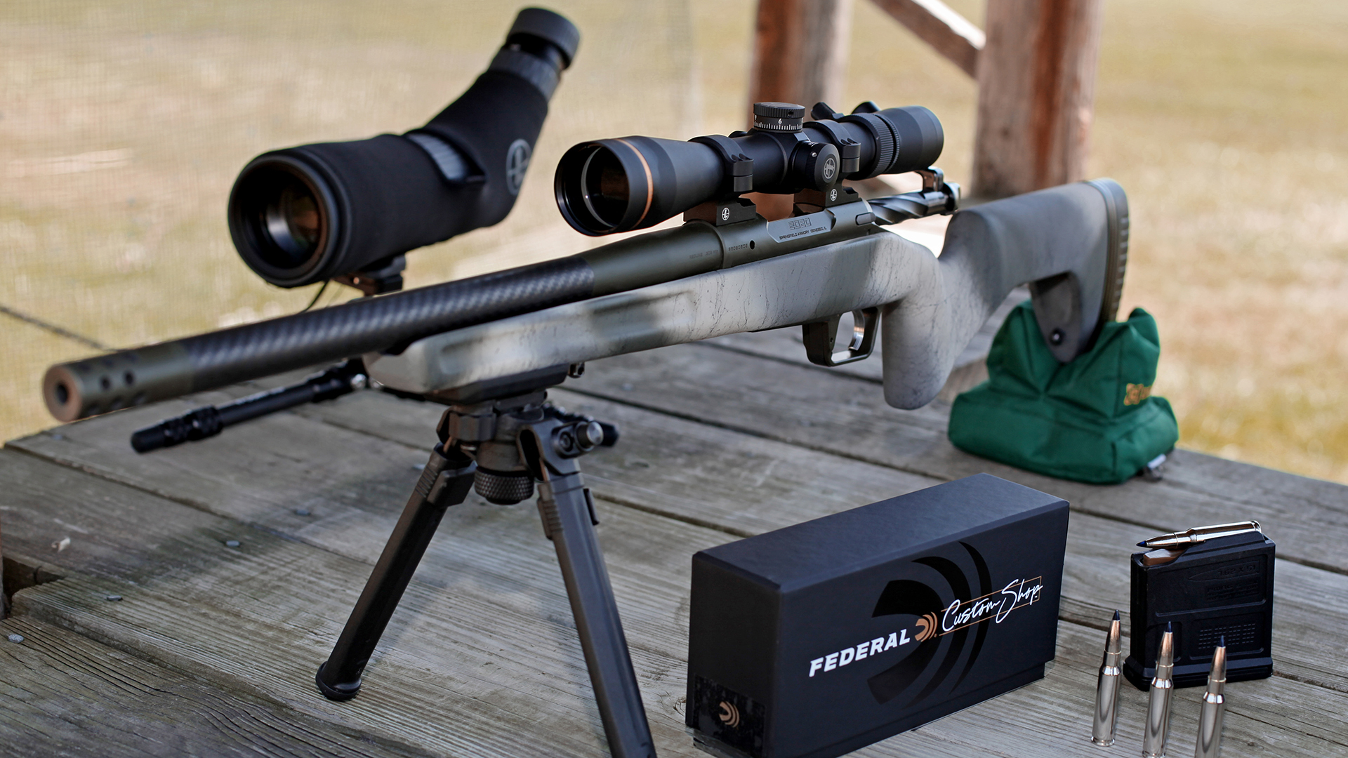 Springfield Armory Redline bolt-action rifle camouflage grayboe stock leupold riflescope on bench shooting range with ammunition spotting scope rear sandbag