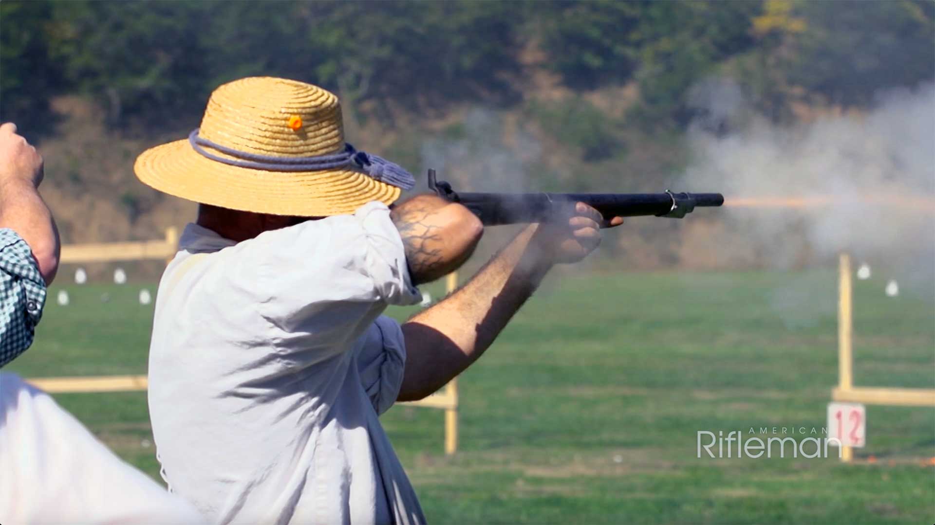 Man in white shirt and straw hat firing a smoothbore musket.