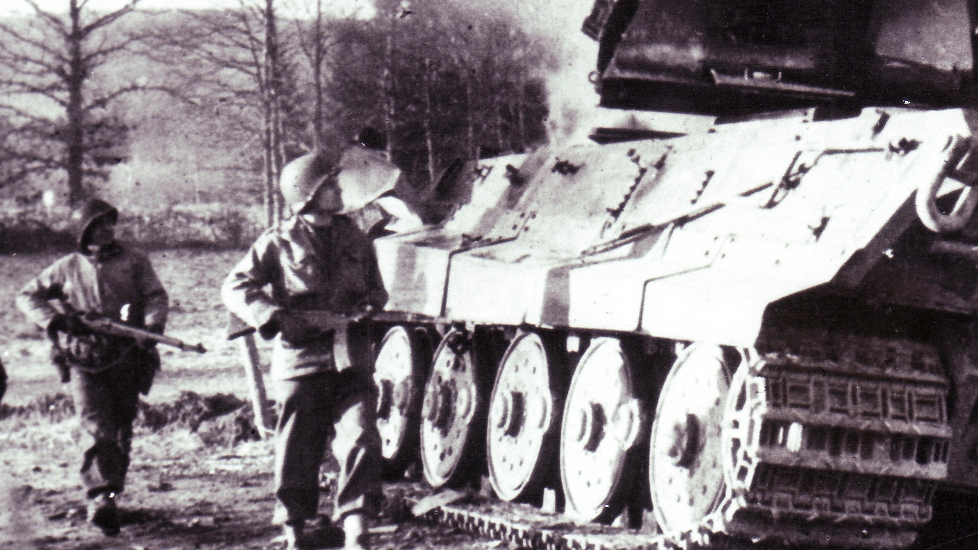 A GI armed with a captured StG44 passes a smoldering German Tiger II (Tiger Ausf. B) near La Gleize, Belgium during late December 1944.
