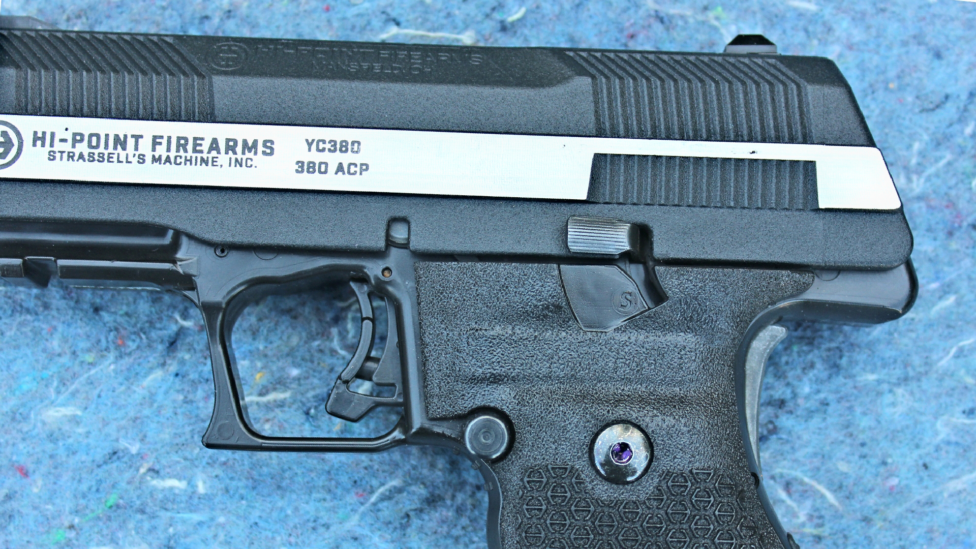 Hi-Point Firearms YC380 pistol left-side view gun closeup controls safety magazine release trigger two-tone metal slide with serrations for gripping shown on speckled blue background