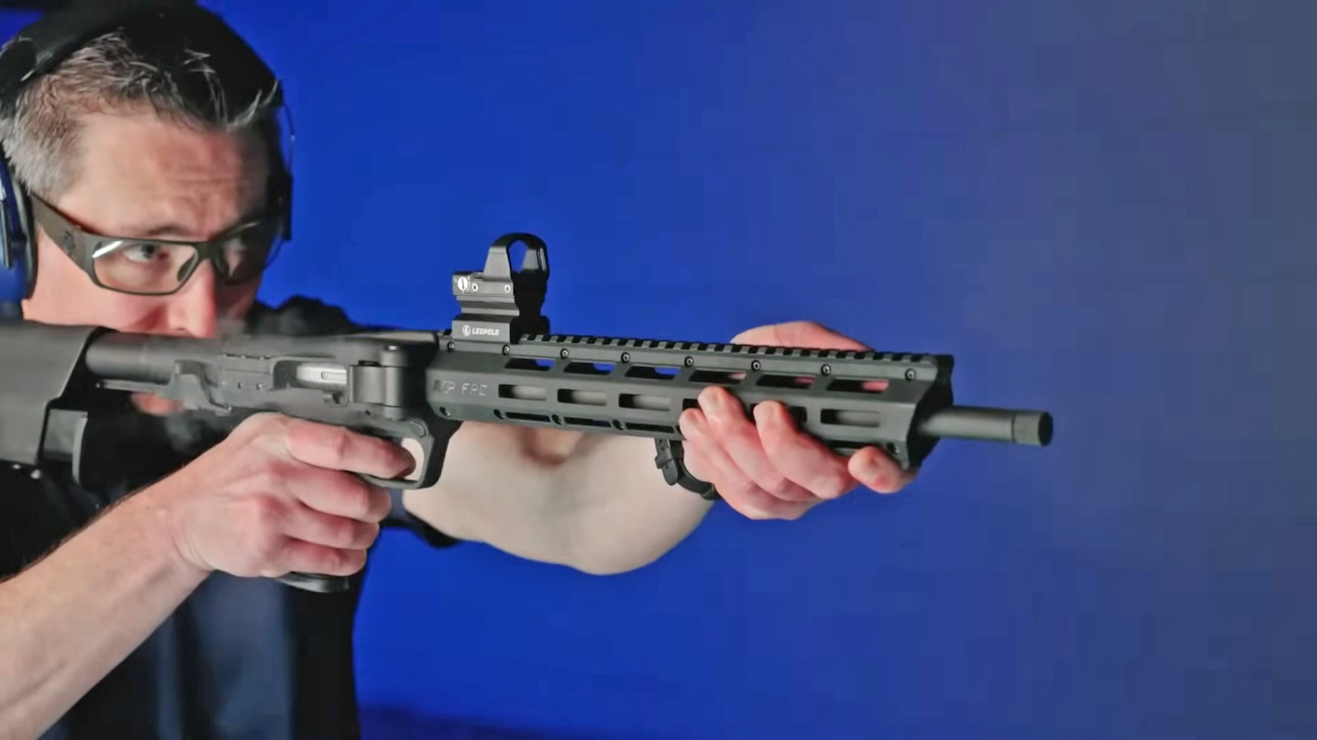 Man shooting the Smith & Wesson FPC carbine in front of a blue range wall.