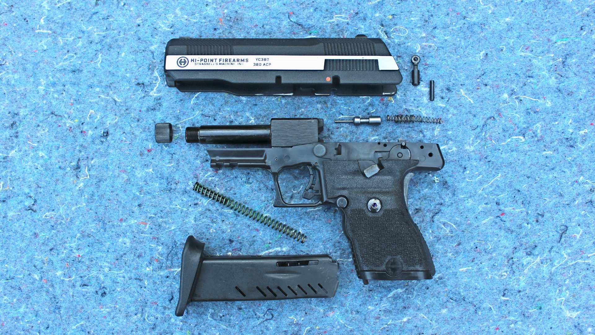 Hi-Point Firearms YC380 yeet cannon pistol 9 mm gun disassembled view parts arrangement slide frame barrel pins springs magazine shown on speckled blue background