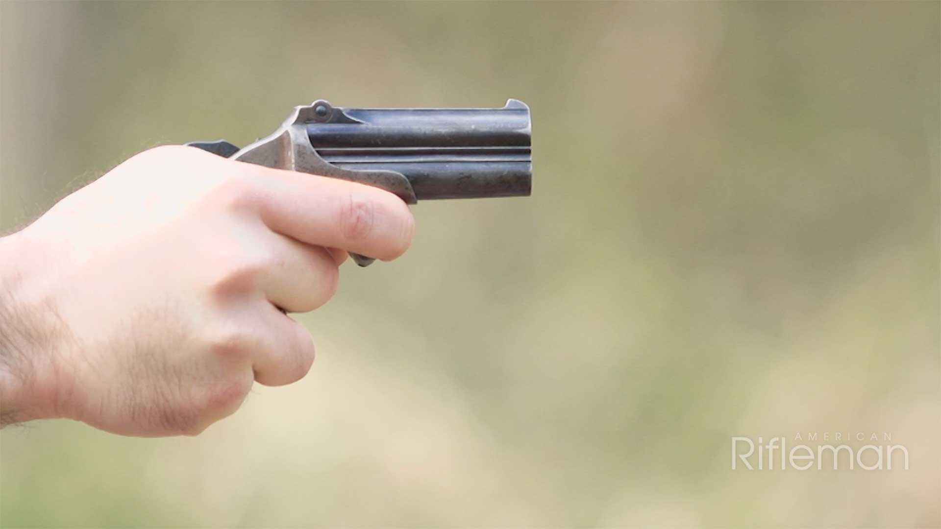 Man aiming the Remington Model 95 Double Derringer on an outdoor range.