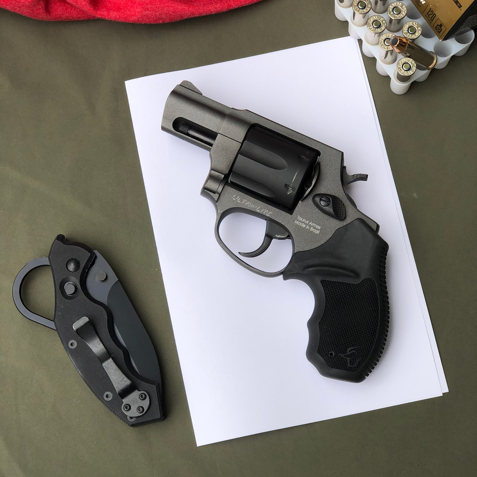 Snub-nose revolver black gun shown on white paper target with knife and ammunition