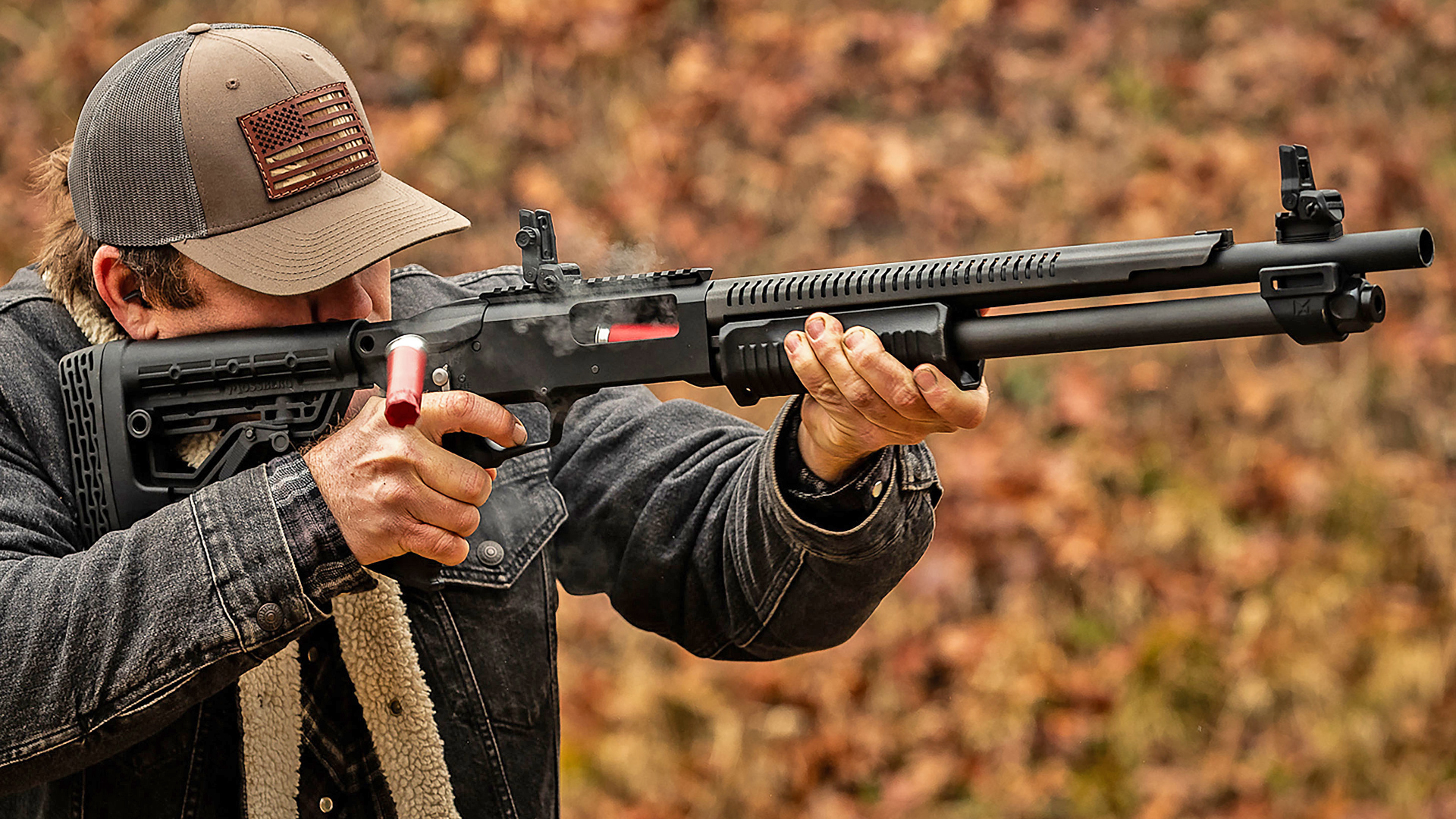 New For 2025: Mossberg 590 rotary safety lever shotgun pump-action being fired outdoors by man shown with action open and shell mid-air