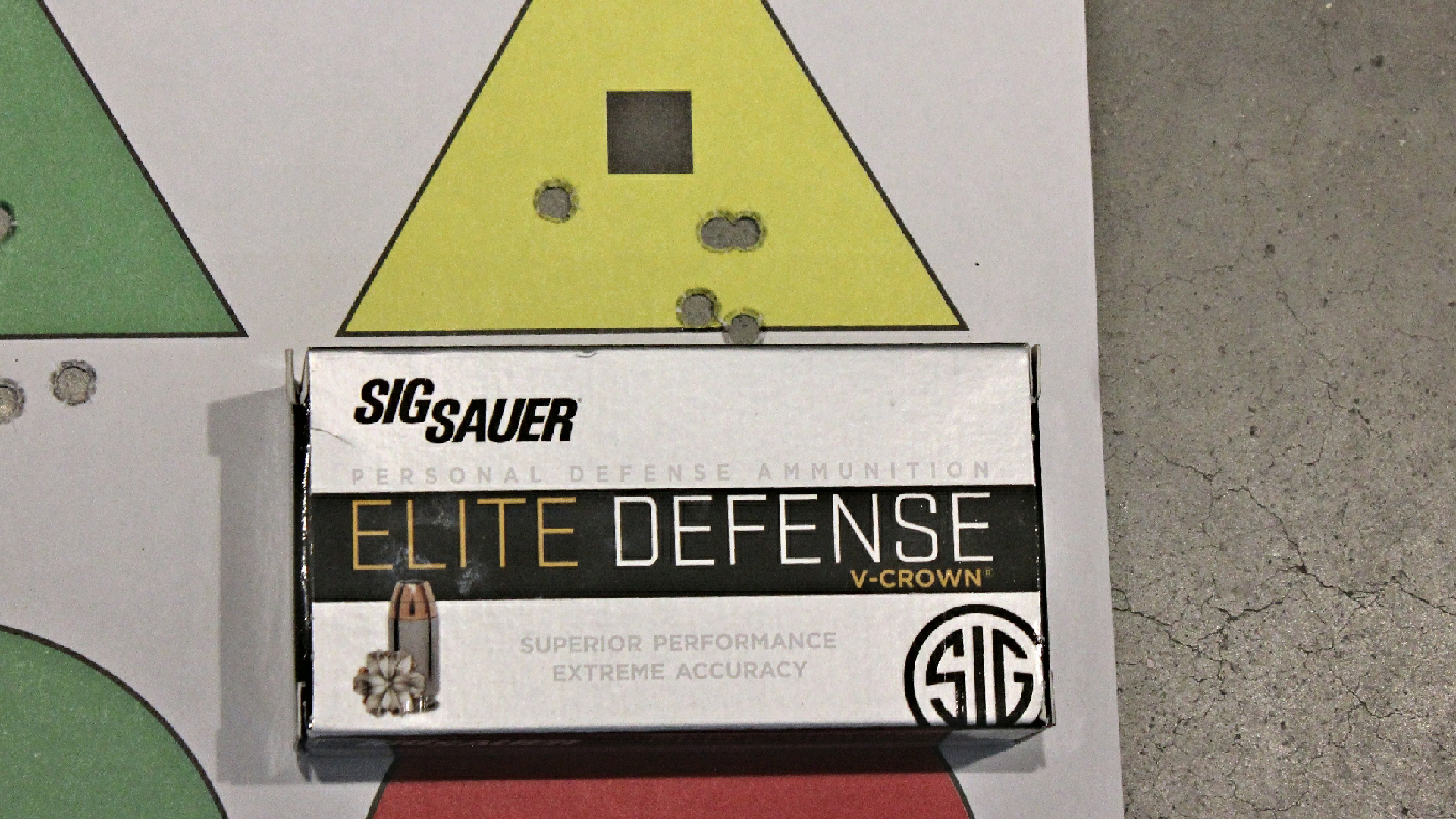 SIG Sauer Elite Defense ammunition box shown on triangle target with bullet holes accuracy group target