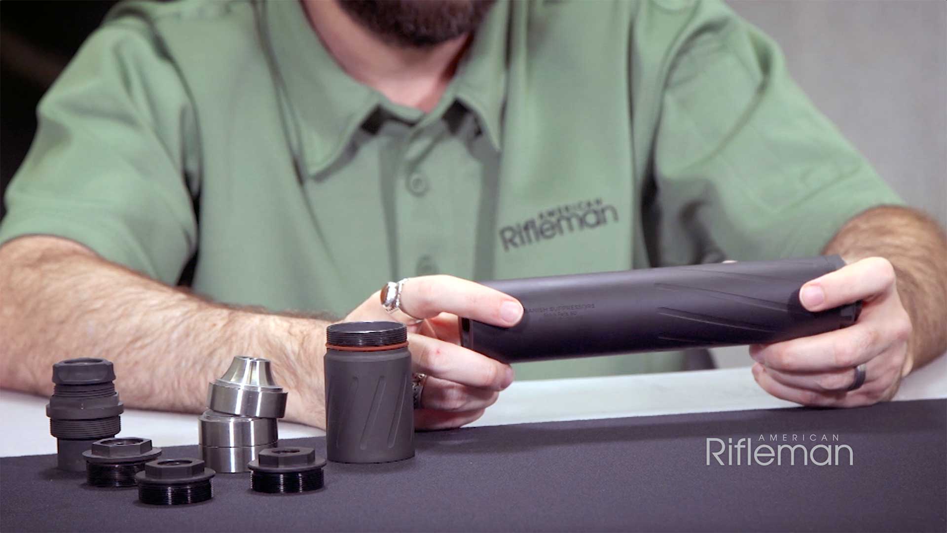 A man in a green shirt displays the black Silencer Central Banish 46 suppressor on a table.