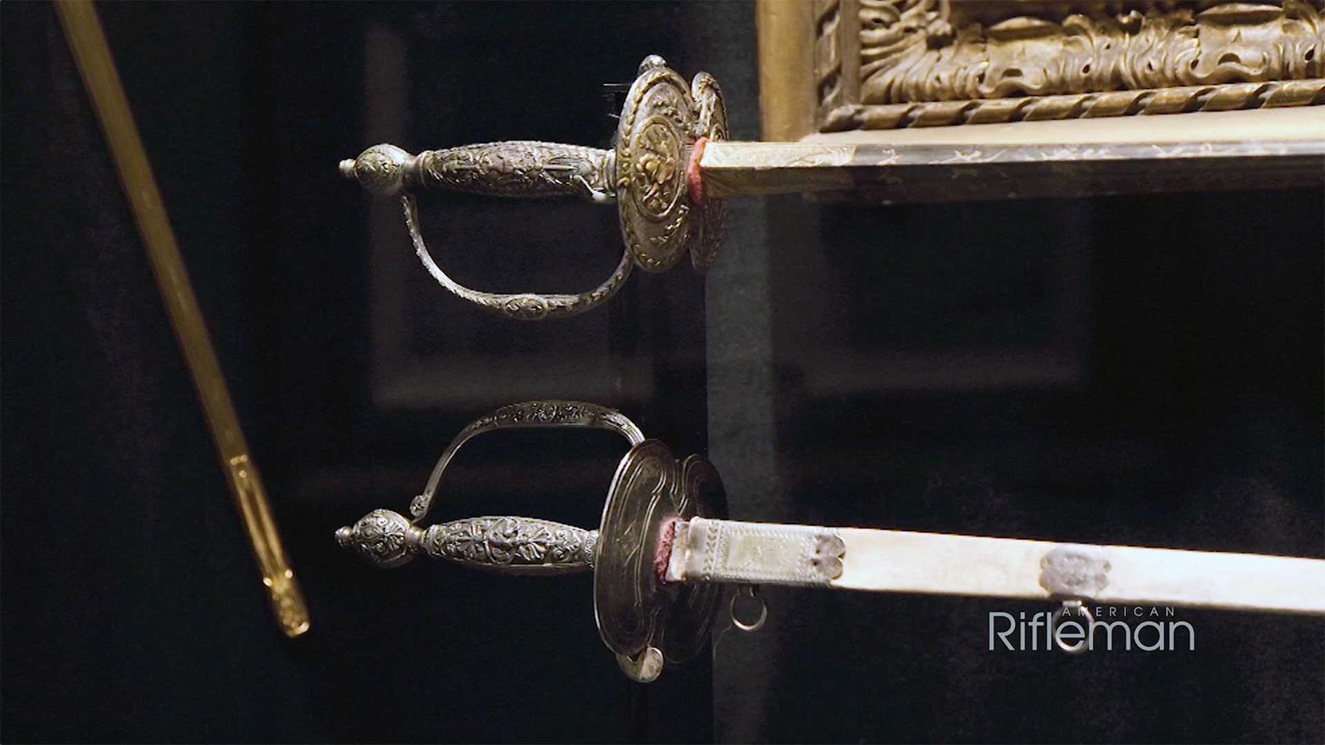 The hilt of two swords in a black-backed museum display case.