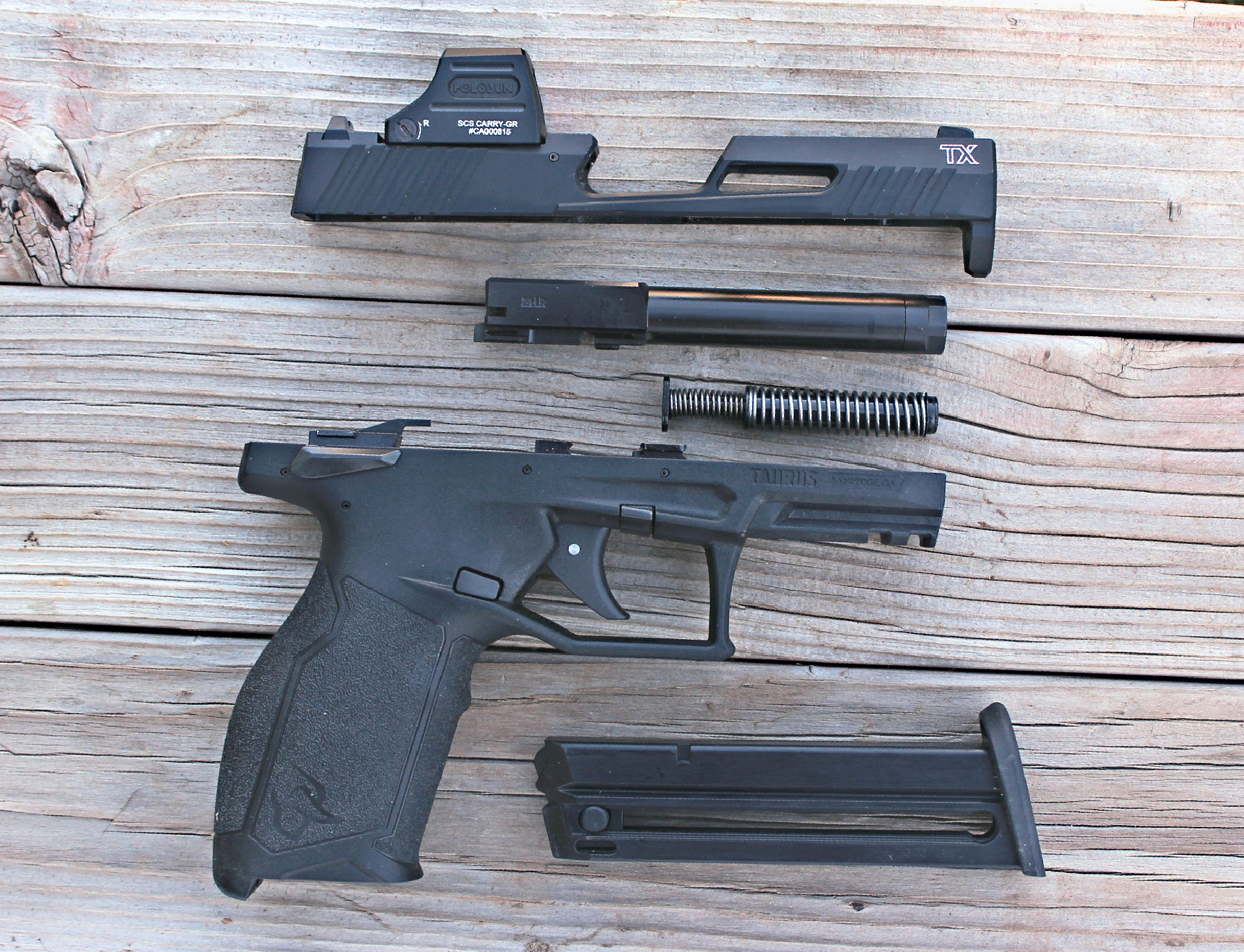 Taurus TX22 T.O.R.O. Black .22LR right-side view disassembled parts slide barrel spring frame magazine shown on wood background