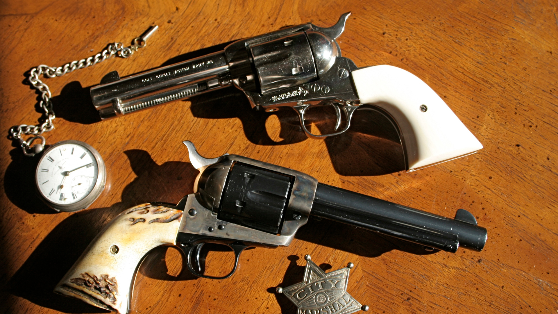 Two colt single-action army revolvers on wood table shown with pocket watch and city marshal star badge