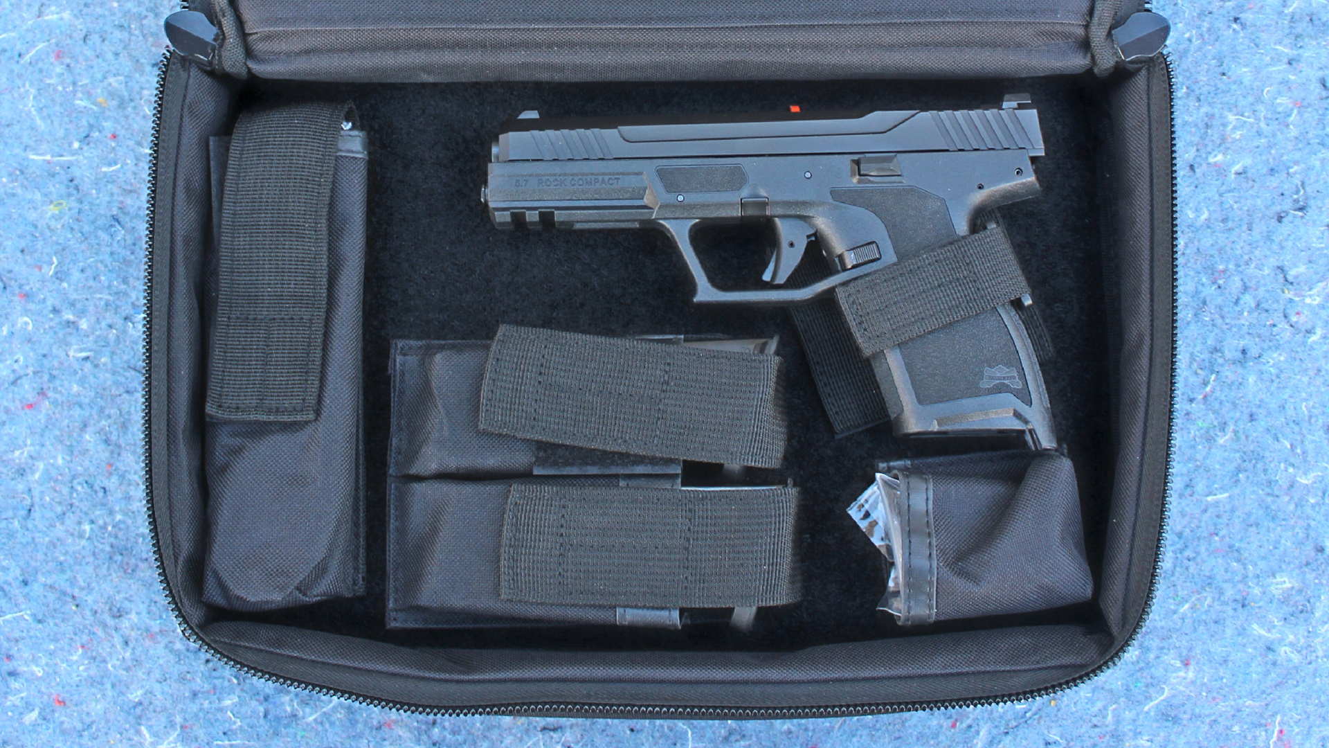 Palmetto State Armory 5.7 Rock Compact pistol in zipperd nylon case hook and look straps compartments pouches magazines chipped blue stone background