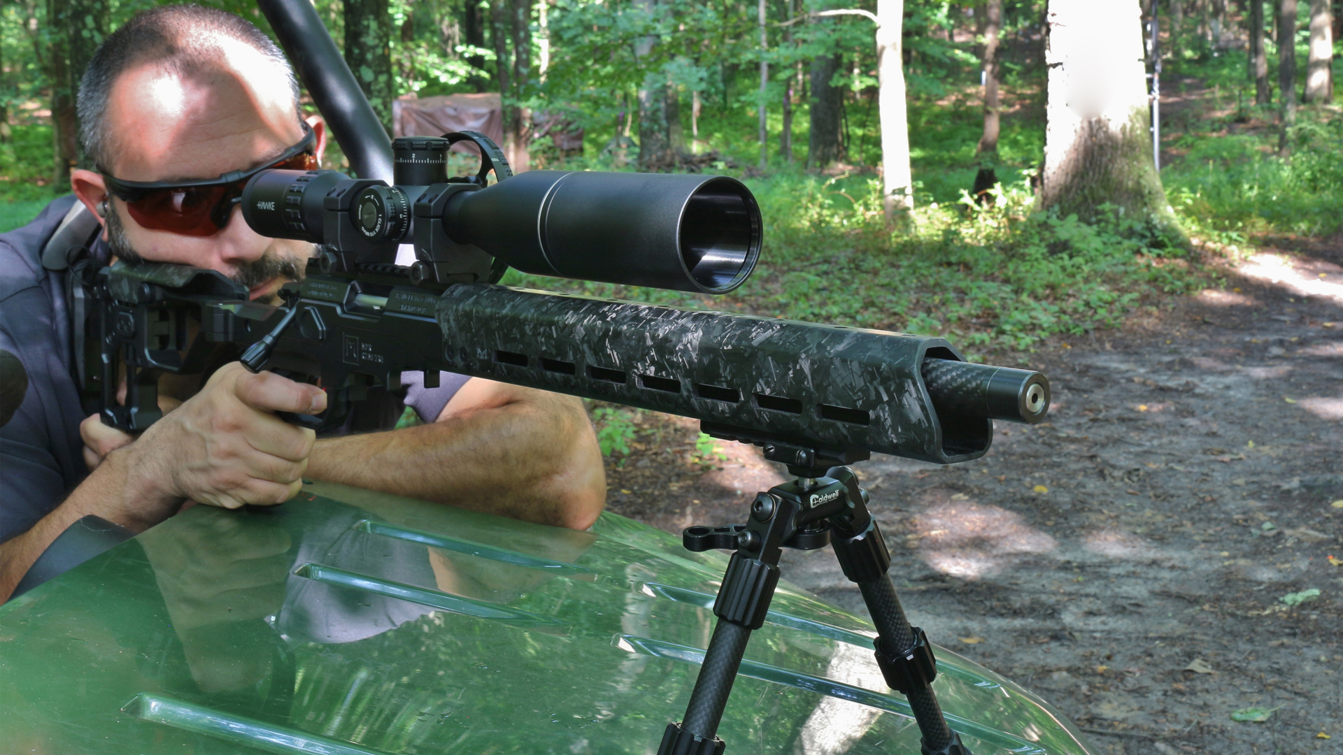 Author Frank Melloni leaning on utility vehicle green hood outdoors shooting christensen arms precision rimfire rifle on bipod over hood