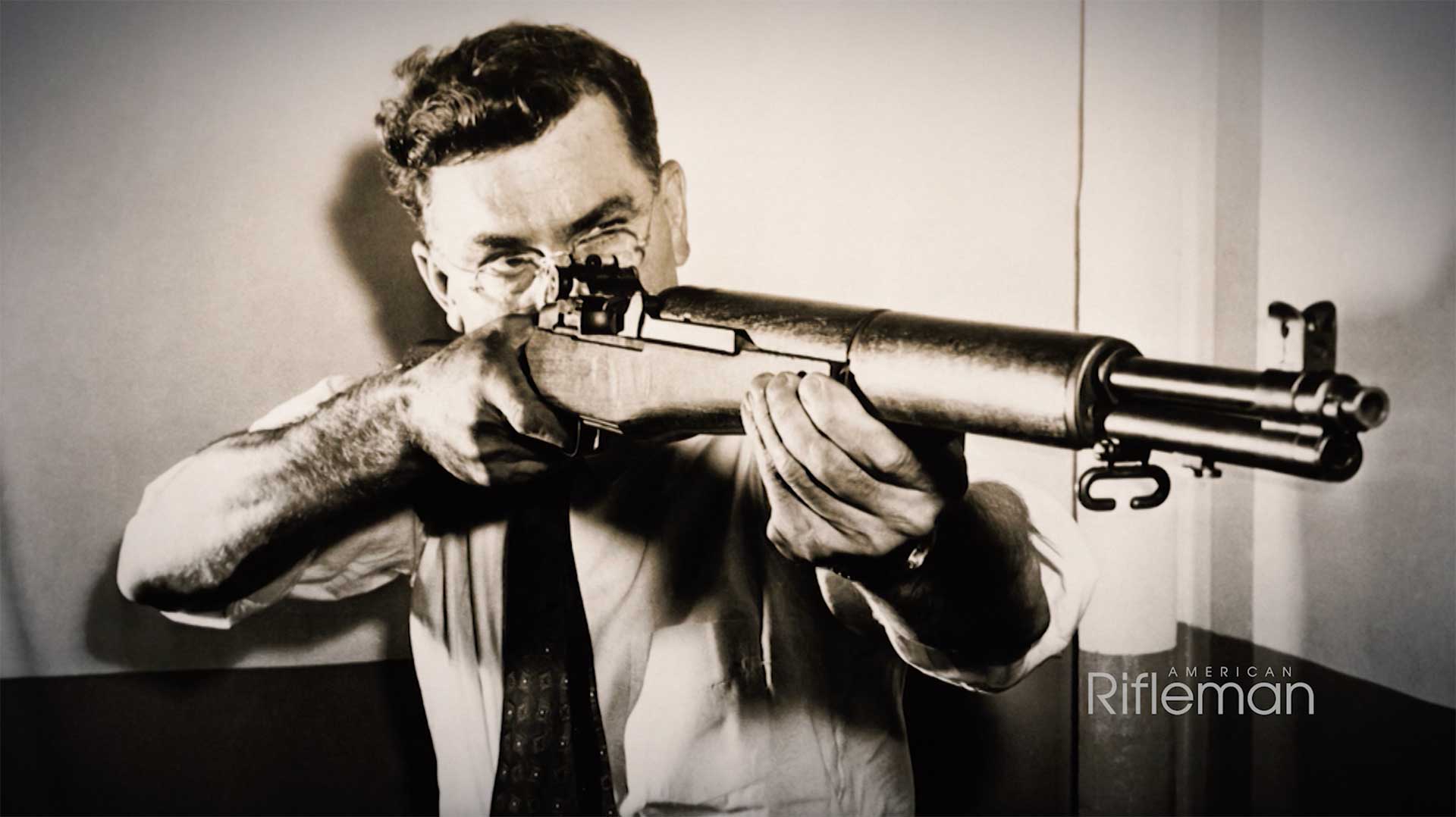 John C. Garand aiming his M1 Garand rifle in a black-and-white historical photograph.