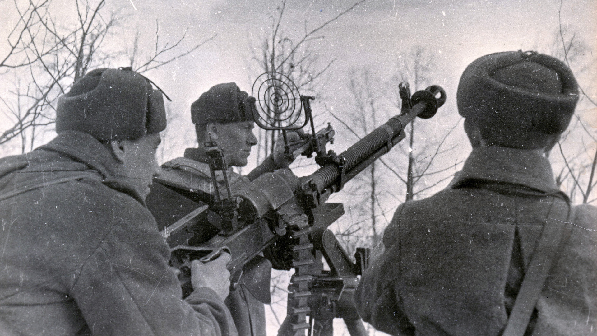 heavy machine gun crew with DShK on tripod pointing in air above trees