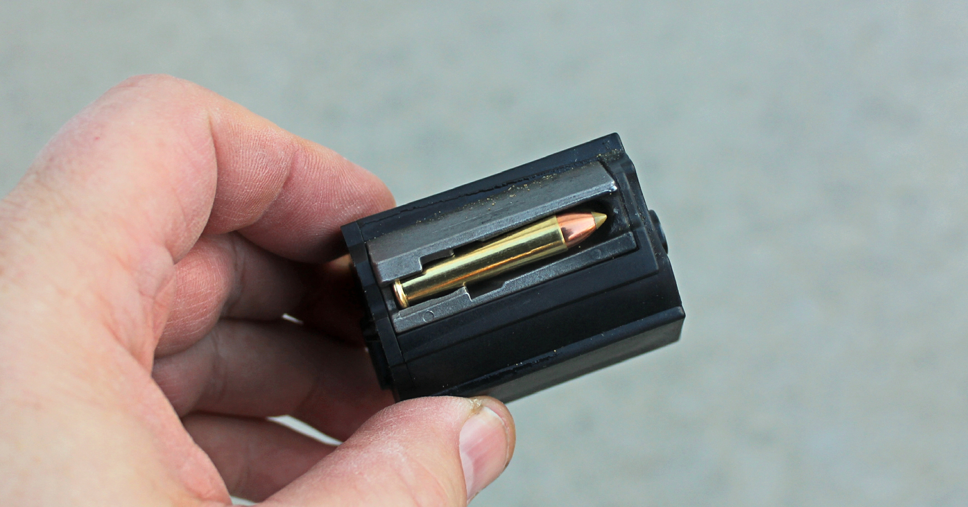 Black rotary magazine held between fingers showing .22 WMR cartridge within