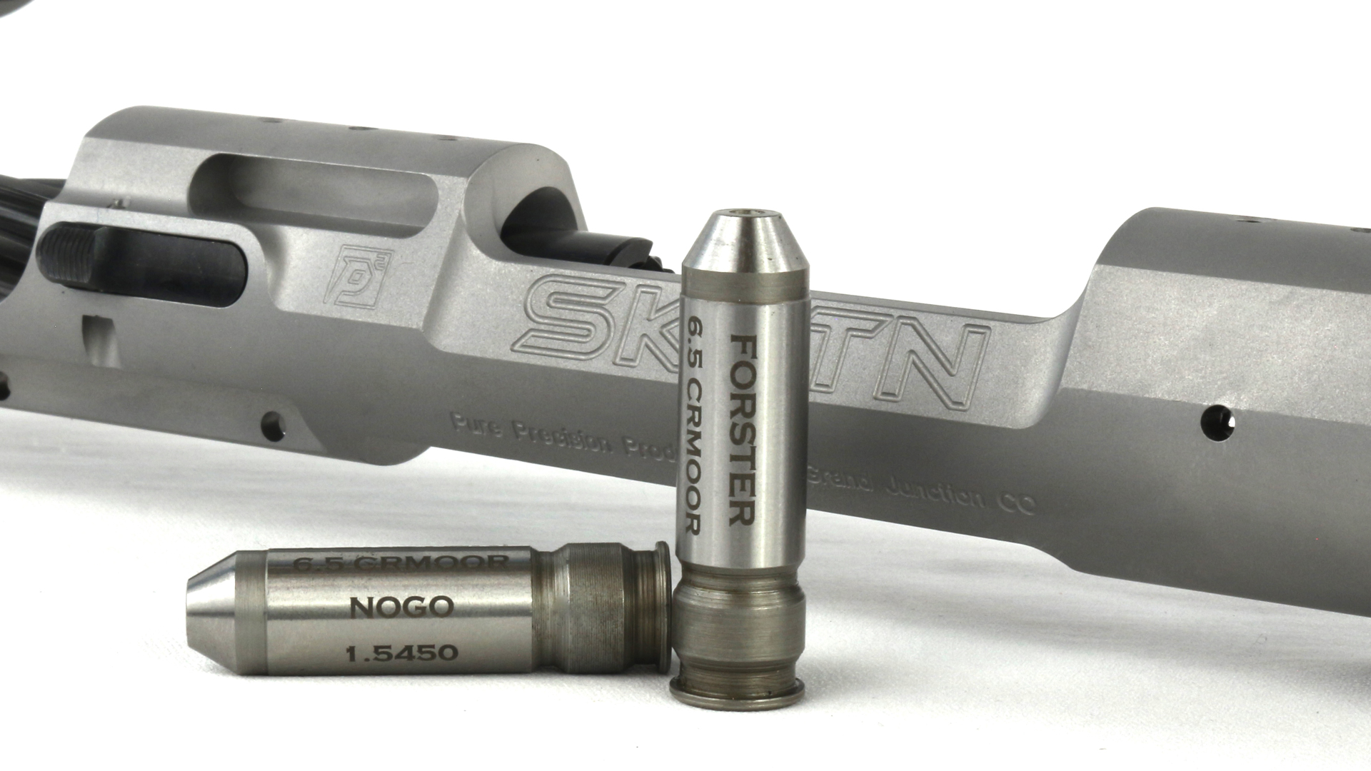 Forster NOGO and Go gauge for 6.5 mm Creedmoor ammunition shown in front of stainless steel rifle receiver