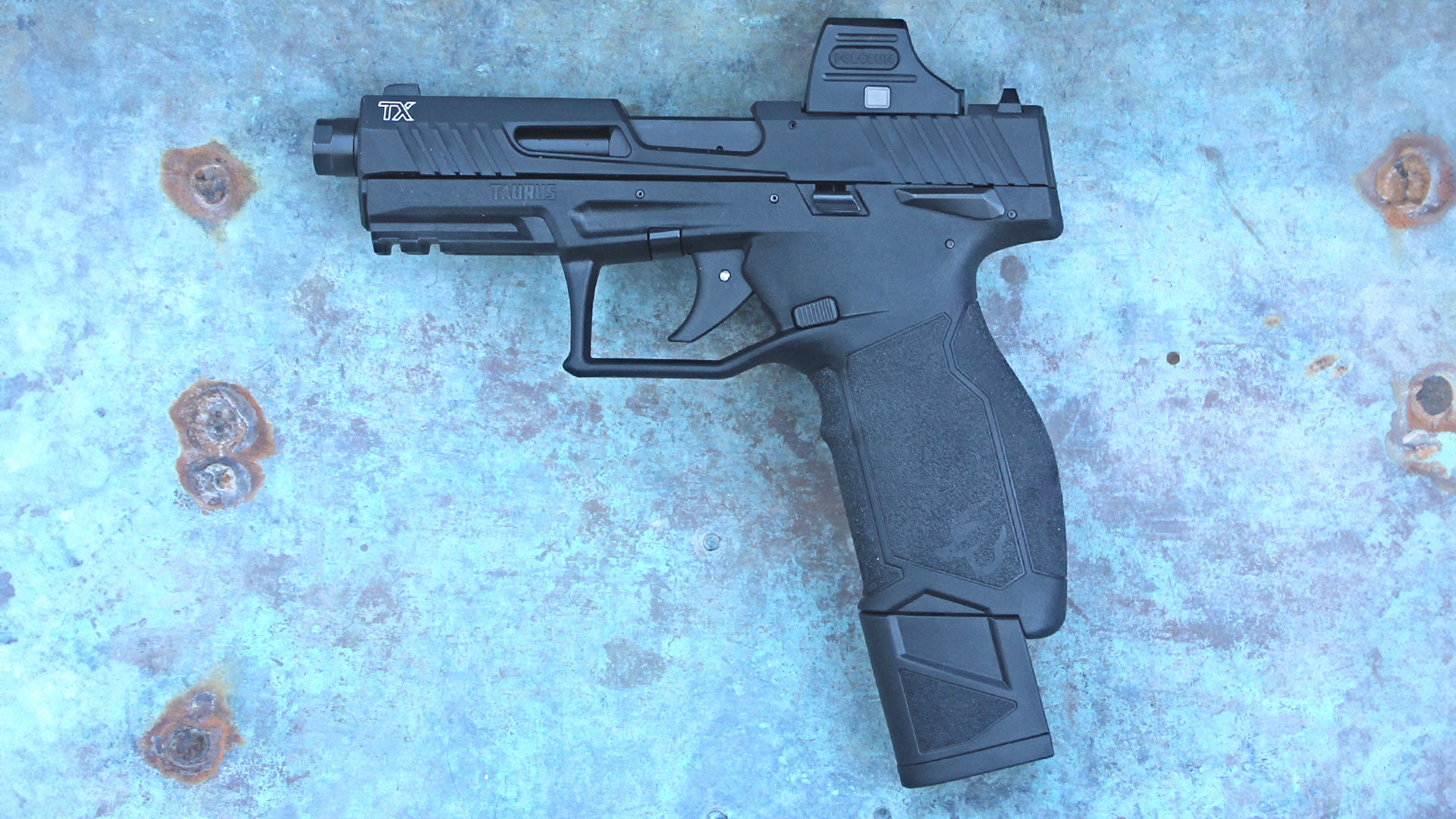 Taurus TX22, left side view, black pistol with extended magazine, Holosun optics, attached rusty steel background