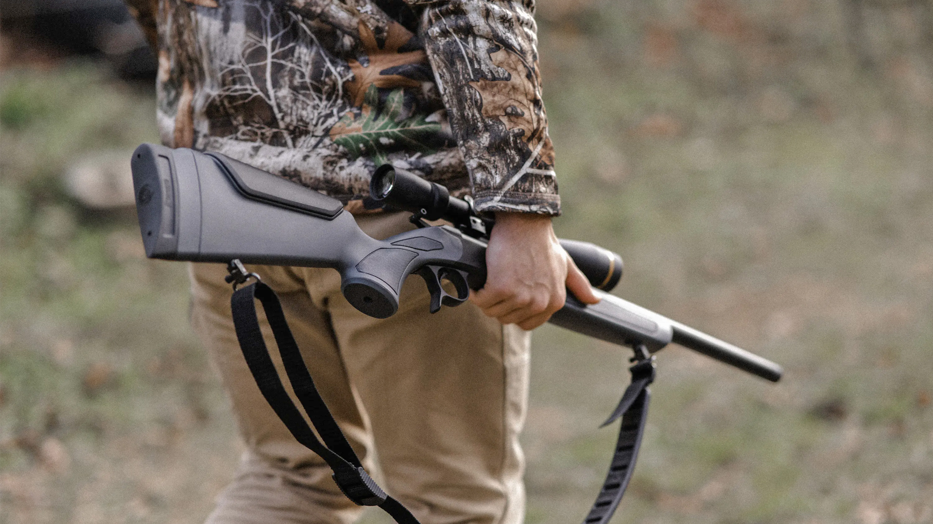 Hunter carrying a CVA Scout rifle at his side while walking into the woods.