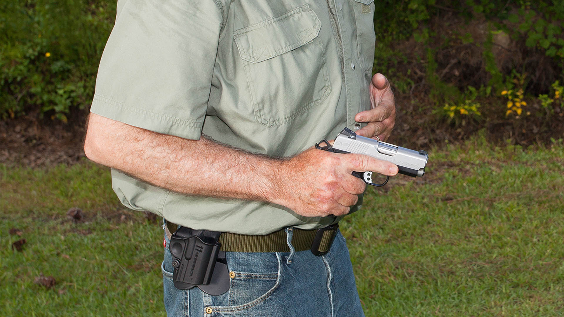 Man with pistol drawn from holster signifying self-defense scenario outdoors