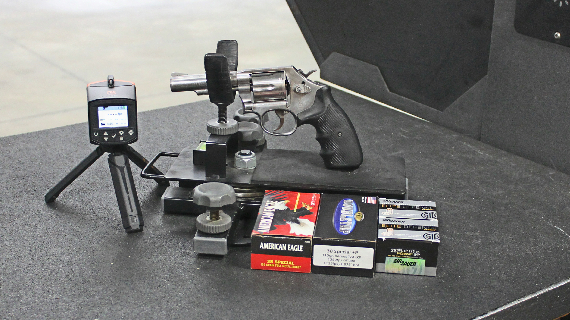 Smith & Wesson Model 64 stainless steel revolver with black rubber stocks in cradle shooting rest on range with boxes of ammunition and LabRadar LX chronograph on tripod left side