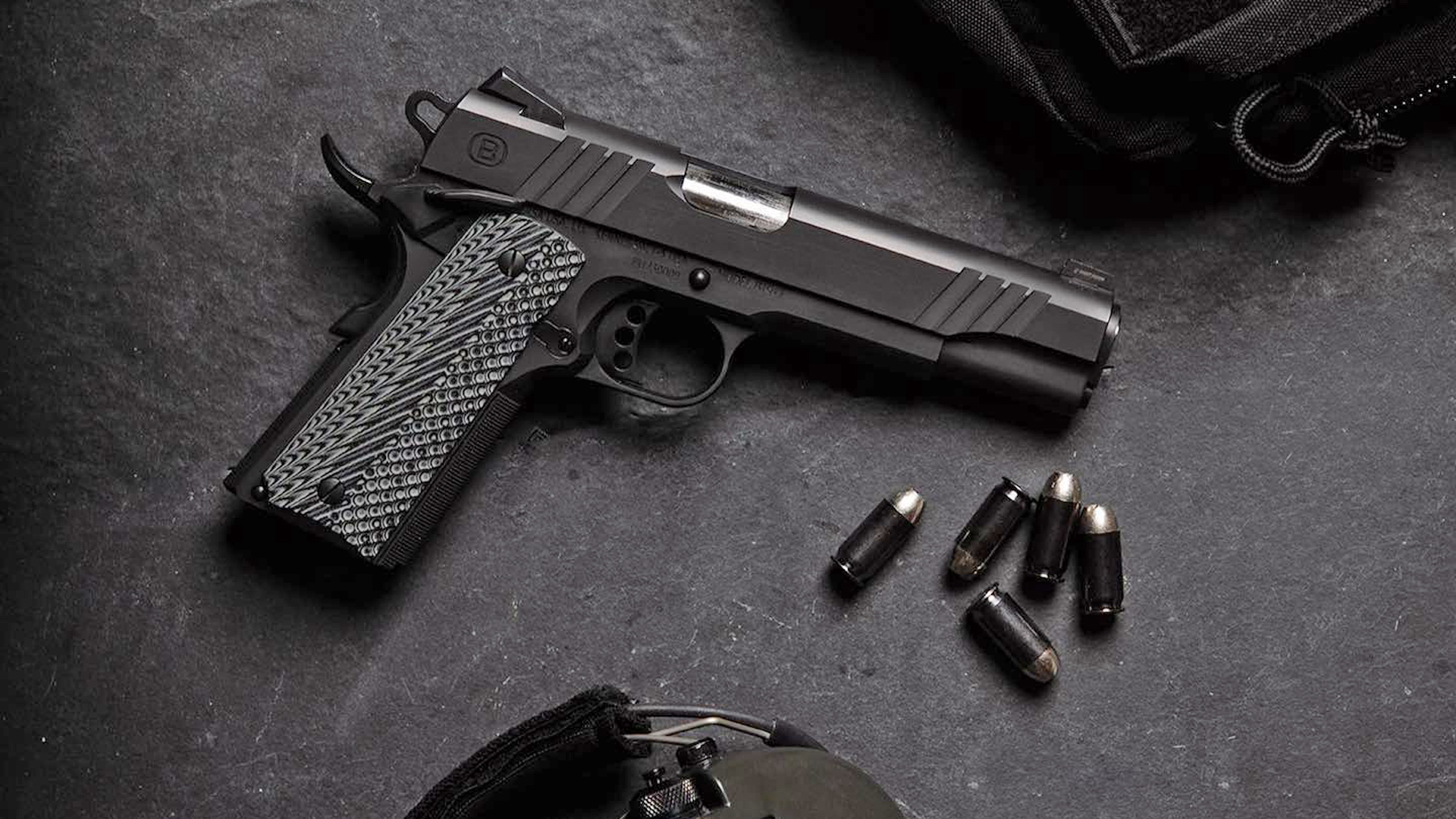 Right side of the all-black Bersa B1911 on a slate background next to .45 ACP ammunition.